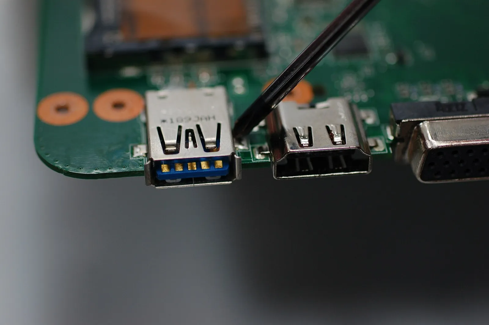 Probe testing solder points beside the USB port on a laptop motherboard